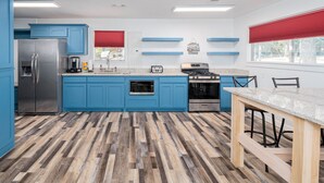 Une cuisine moderne avec des meubles bleus, un réfrigérateur en acier inoxydable, une cuisinière à gaz et une table à manger en bois.