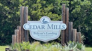 Une enseigne indiquant l’emplacement de Cedar Mills Marina & Resort et du restaurant Pelican’s Landing, situé au bord de l’eau, le tout entouré de poteaux en bois et de verdure.