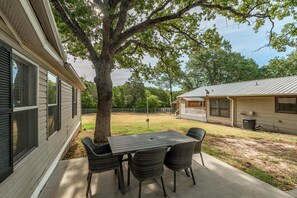 Une terrasse avec une table et des chaises, un arbre et une maison avec un porche.