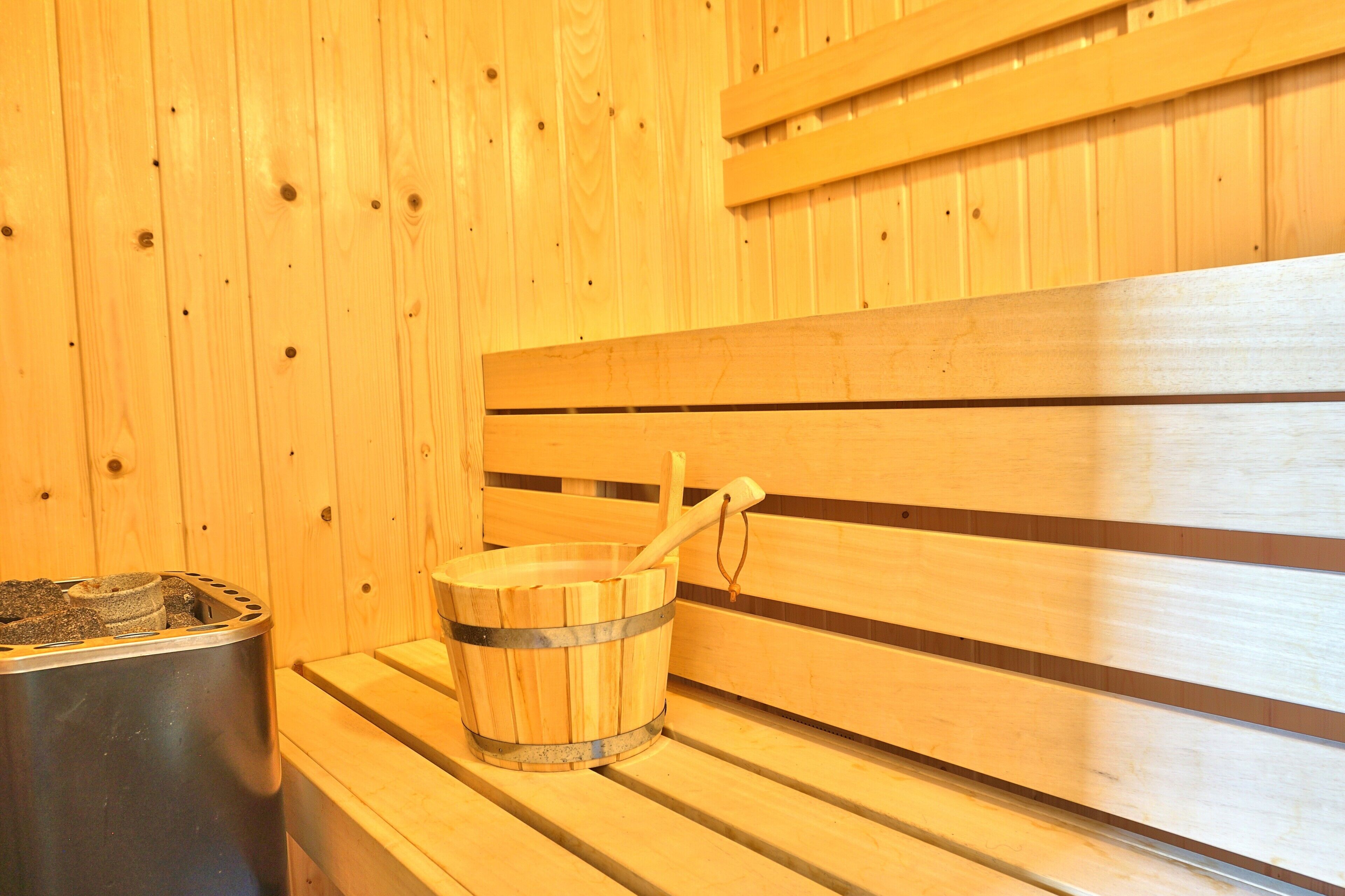 A wooden sauna bench with a bucket and a wooden mallet.