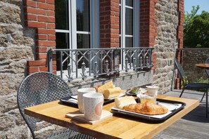 A wooden table with a tray of food, including croissants and a sandwich, and two cups on a balcony with a stone wall and metal railing in the background. - Auberge Ti'gousket (Guingamp)