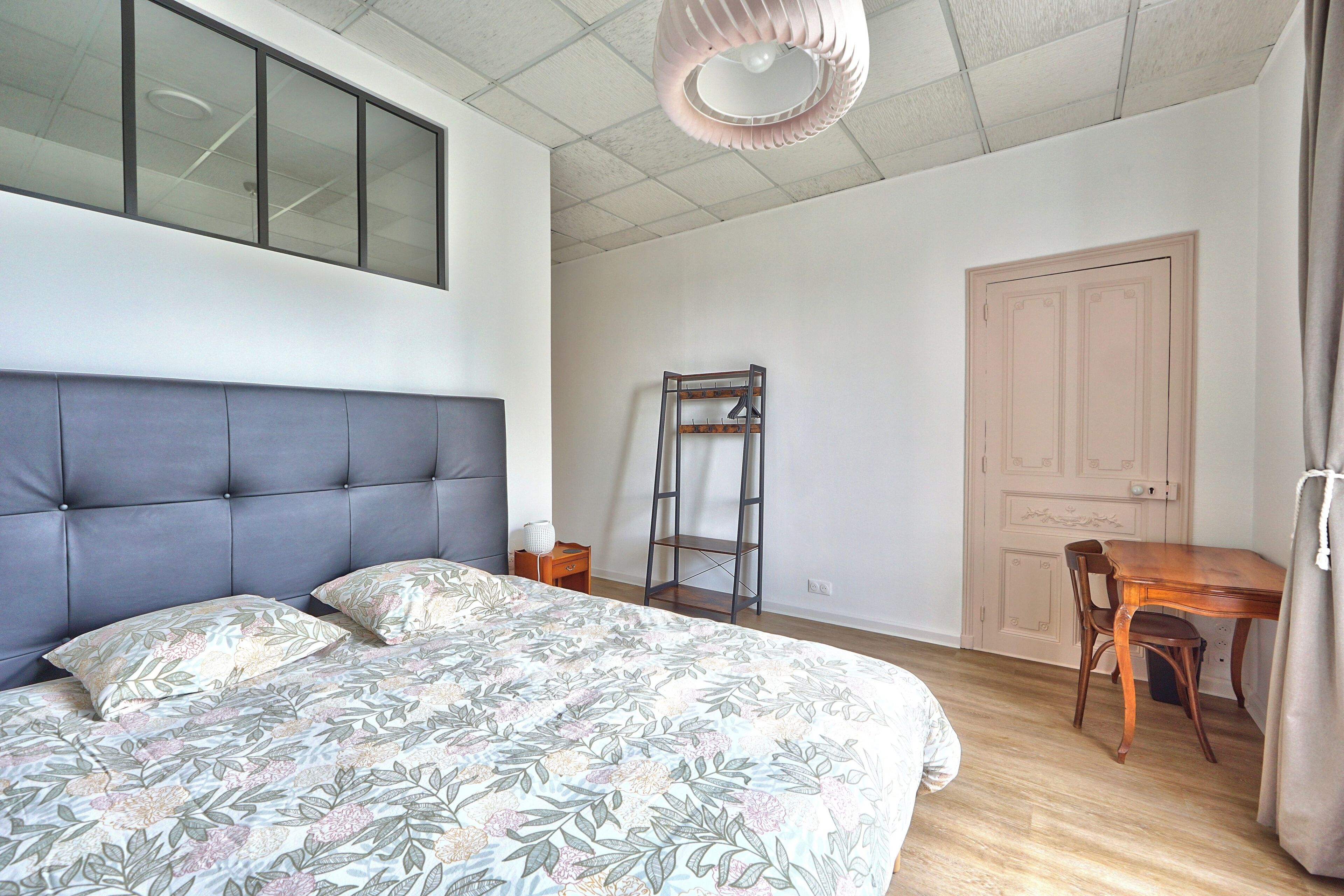 A bedroom with a bed, a wooden desk, a ladder, and a door.