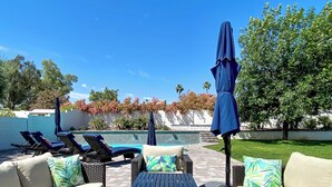 Un patio con piscina, sillas de descanso y una mesa con cojines.