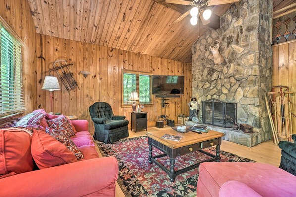 A cozy living room with wooden walls, a stone fireplace, a plush red sofa, and a television. - Serene Sky Valley Family Chalet w/ Fireplace (Sky Valley)