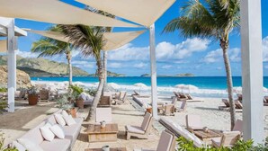 A beachside lounge with sun loungers and umbrellas, overlooking a clear blue sea and sandy beach. - Front line unit 520 ft2 on 2nd floor facing ocean (Orient Bay)