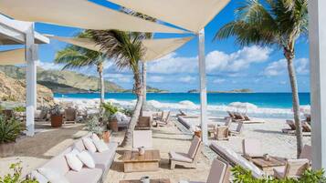 Un salon de plage doté de chaises longues et de parasols, offrant une vue sur une mer bleue et une plage de sable fin.