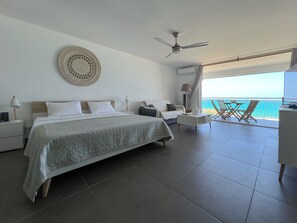 Habitación de hotel con cama, mesitas de noche, lámpara, ventilador de techo y balcón con vista al mar.