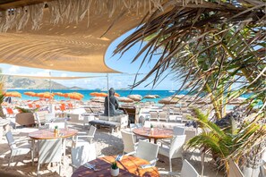 Un restaurante frente al mar con terraza, sombrillas y una estatua.