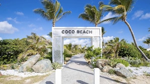 A pathway leading to a sign labeled "COCO BEACH" with palm trees and rocks in the background. - Front line unit 520 ft2 on 2nd floor facing ocean (Orient Bay)