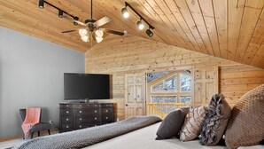 Un dormitorio con una cama, un aparador, un televisor y techo de madera.
