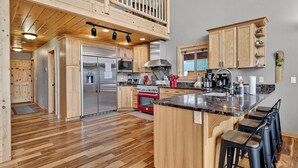 Una cocina amplia con armarios de madera, un refrigerador de acero inoxidable, un horno rojo y una encimera de mármol.