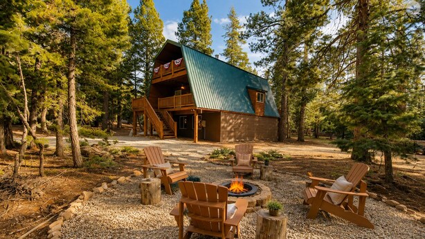 A cabin with a fire pit and outdoor seating, surrounded by trees.
