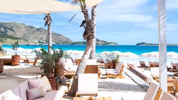 A beachside lounge with wooden furniture, potted plants, and umbrellas.
