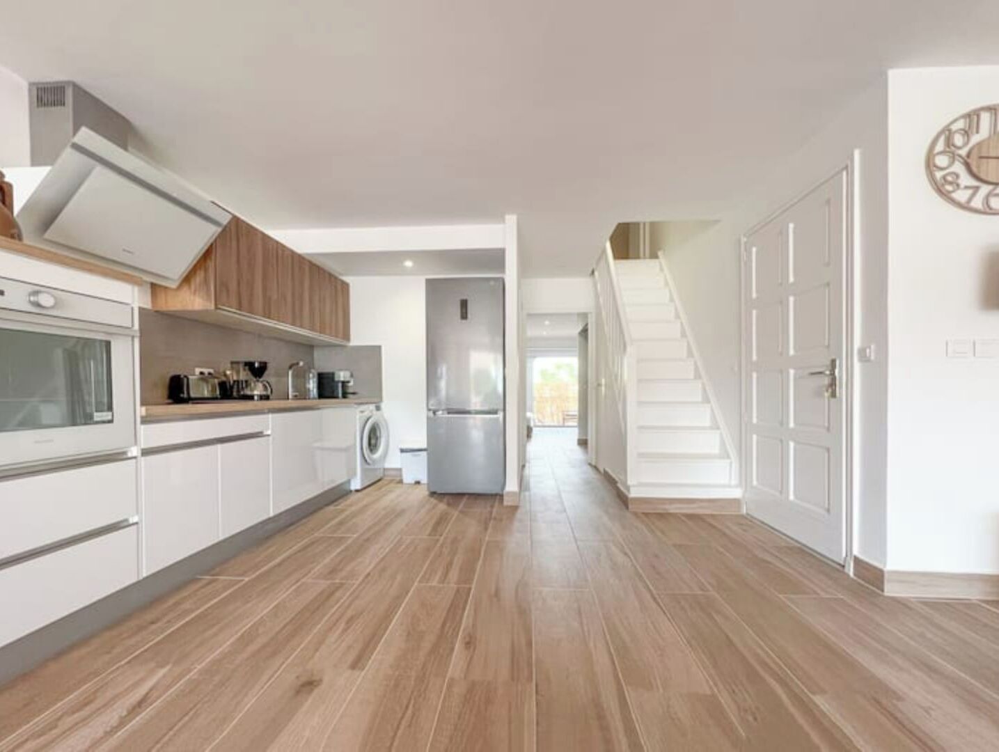 Una cocina moderna con armarios blancos, horno empotrado y refrigerador de acero inoxidable.