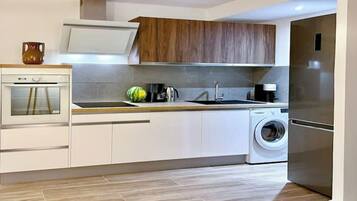 A modern kitchen with a built-in oven, a sink, a washing machine, and wooden cabinets.
