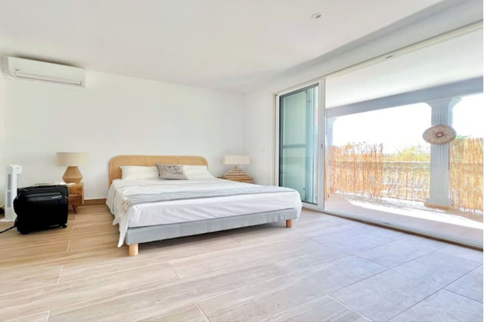 Een moderne slaapkamer met een groot bed, een koffer en een schuifglazen deur naar een balkon.