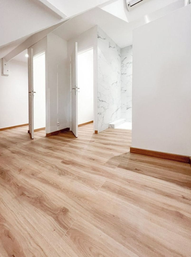 A spacious room with wooden flooring, white walls, and a marble accent wall.