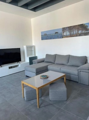 Una sala de estar moderna con un sofá seccional gris, un televisor de pantalla plana, una mesa de centro de vidrio y un cuadro en la pared.