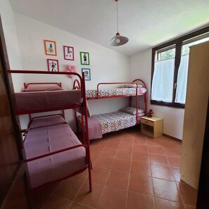A dormitory room with bunk beds, a small bedside table, a window with curtains, and wall decorations.