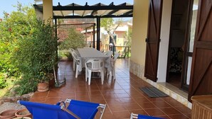 A covered patio with a table and chairs, potted plants, and a view of the surrounding area. - Sicicas, 300 meters from the sea, 5 minutes walk (Villasimius)