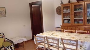 A dining area with a table set for four, a wooden cabinet with glass doors, and a patterned tablecloth. - Sicicas, 300 meters from the sea, 5 minutes walk (Villasimius)
