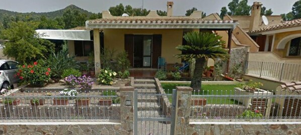 Een wooneiland met een overdekte patio, een stenen hek en diverse planten in potten.