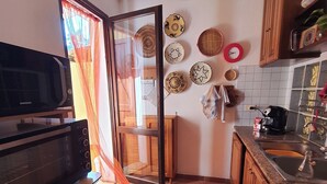 A kitchen with a microwave, a sink, and a stove. There are decorative plates on the wall and a window with curtains. - Sicicas, 300 meters from the sea, 5 minutes walk (Villasimius)