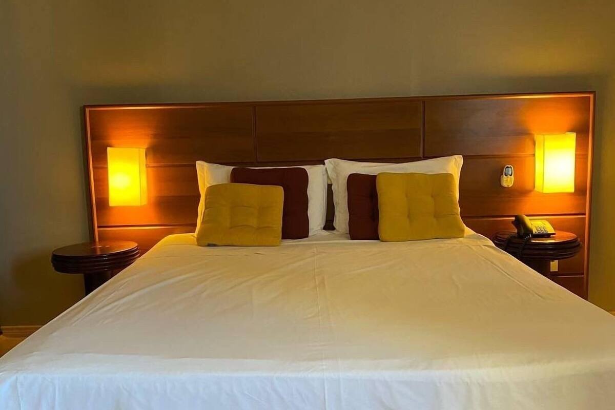 A large bed with white bedding, two nightstands with lamps, and a wooden headboard.