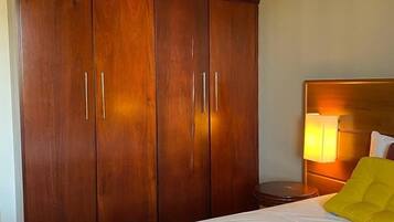 Habitación de hotel con un armario de madera grande, una cama con ropa blanca y una mesita de noche con lámpara.