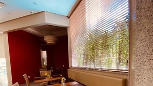 A modern dining area with a booth seating arrangement, a wooden table, and a view through a window with blinds. - Apart-Hotel Prinz (Joinville)