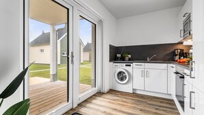 A modern kitchen with a washing machine, a coffee maker, and a wooden deck visible through the glass door.