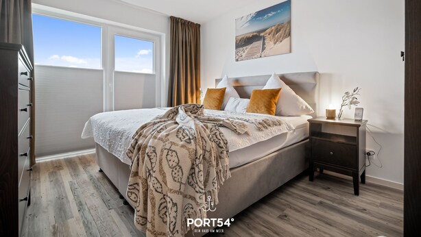A bedroom with a large bed, a nightstand, a window with curtains, and a painting on the wall.