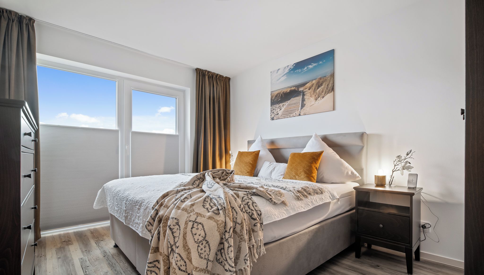 A bedroom with a large bed, a nightstand, a window with curtains, and a painting on the wall.