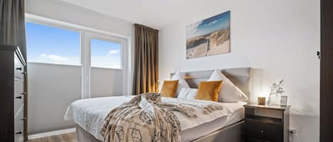 Un dormitorio con una cama grande, una mesita de noche, una ventana con cortinas y un cuadro en la pared.