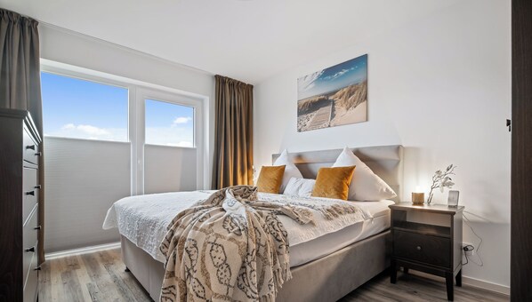 Une chambre à coucher avec un grand lit, une table de chevet, une fenêtre avec des rideaux et un tableau au mur.