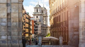 Una strada storica con una torre campanaria imponente, edifici in pietra e un percorso pedonale.