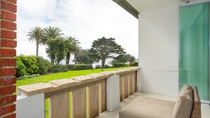A balcony with a view of a well-maintained lawn and palm trees, a white wall, and a glass door. - Sonnekus 5 (Cape Town)