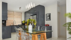 A modern kitchen with a glass dining table, clear chairs, and a central vase with plants. - Sonnekus 5 (Cape Town)