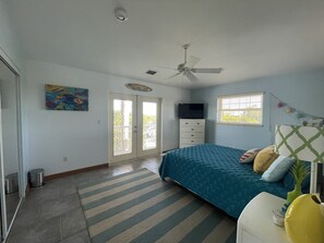 A bedroom with a bed, a ceiling fan, a TV, a window, and a door. - Pool, tiki hut, easy ocean access canal, dock, prime location 30m to Key West (Cudjoe Key)