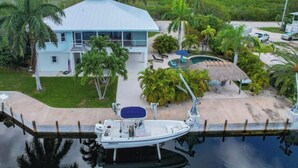 Uma casa com piscina, um barco atracado em frente e vista para o oceano.