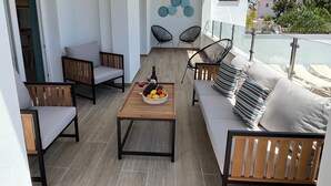 Een balkon met een houten tafel, twee banken en twee stoelen.