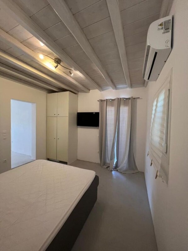 A bedroom with a bed, wardrobe, air conditioning unit, and a television. - Charming Apartment in Ano Mera (Mykonos)