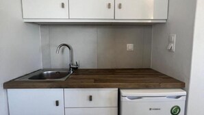 A compact kitchen with white cabinets, a wooden countertop, a stainless steel sink, and a white dishwasher. - Charming Apartment in Ano Mera (Mykonos)