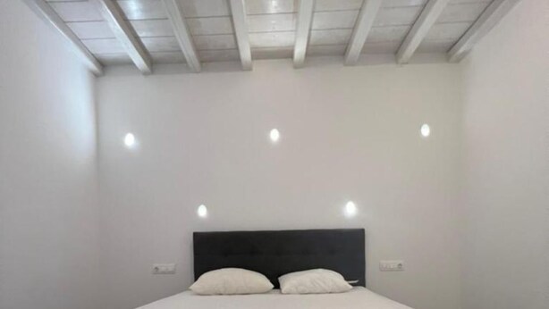 A bedroom with a large bed, white walls, and a sloped ceiling with recessed lighting. - Charming Apartment in Ano Mera (Mykonos)