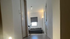 A narrow hallway with a carpeted floor leading to a room with a bed and a window. - Charming Apartment in Ano Mera (Mykonos)