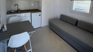A compact kitchenette with a sink, a small refrigerator, and a dining area with a table and chairs. - Charming Apartment in Ano Mera (Mykonos)