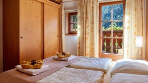 A room with two beds, a wooden wardrobe, a window with curtains, and a small table with a lamp. - Apartment "Linde - Fiechterhof" with Shared Open Terrace, Garden & Wi-Fi (Sarentino)