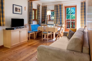 Un salon comprenant un canapé, une table à manger avec des chaises, un téléviseur et une fenêtre avec des rideaux.