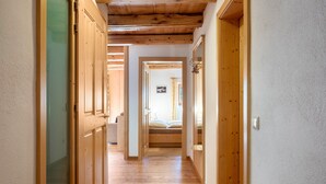 Un couloir en bois, avec un lit au fond, une porte à gauche et un interrupteur à droite.