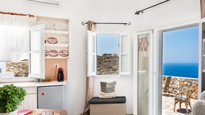 Un balcón con vista al mar, un banco de mimbre, una mesa con una planta en maceta y una silla.